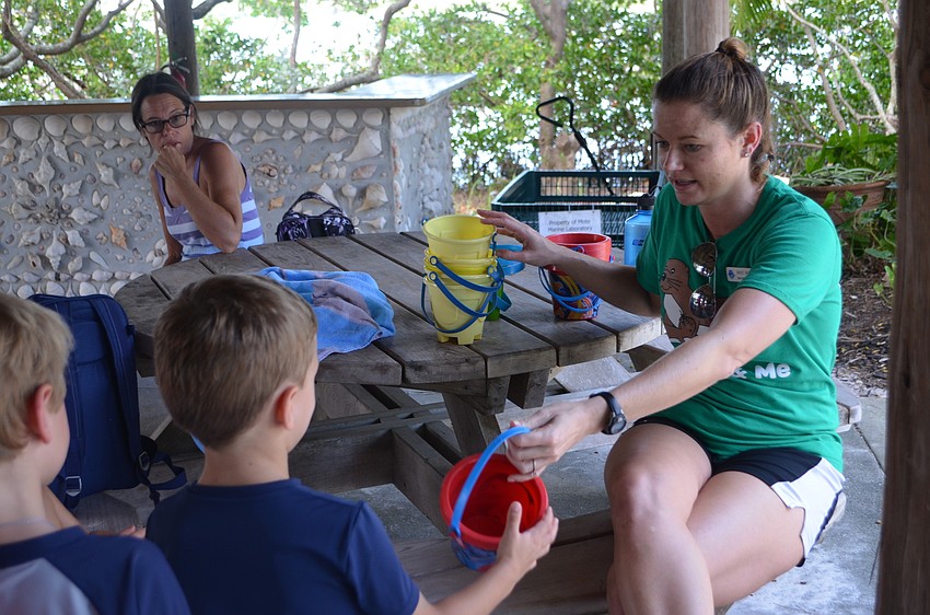 Public Programs Coordinator Miranda Wrobel hands out buckets to campers so they can carry the tiny creatures they find while skimming the bay.