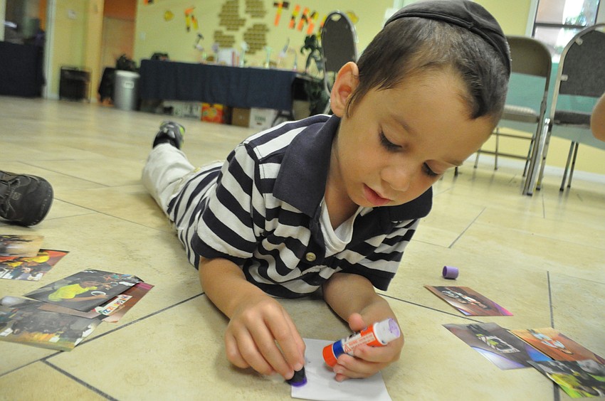 Shua Bukiet, 6, makes himself comfortable as he looks through pictures from the week and glues them to a display board.