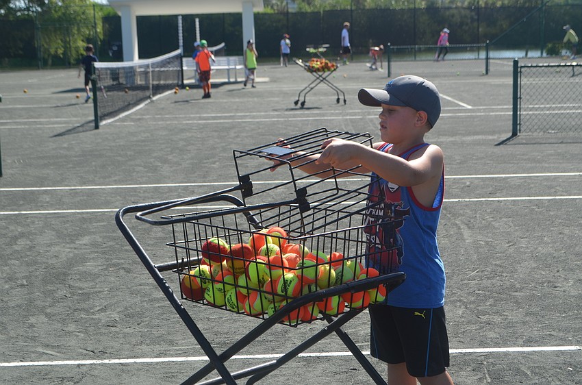 Dylan McLeod, 6, puts tennis balls back in the basket after completing a drill.