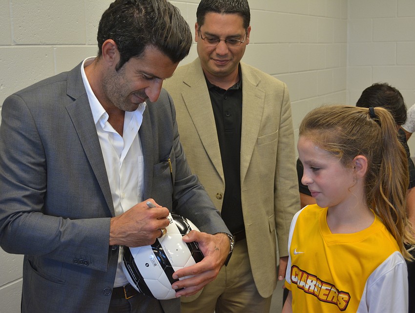Luis Figo signs a ball for Lakewood Ranch's Brinley Beorlegui on her 10th birthday. Carlos Vallejo, who will be Figo's tournament director when it comes to Lakewood Ranch in November, watches.