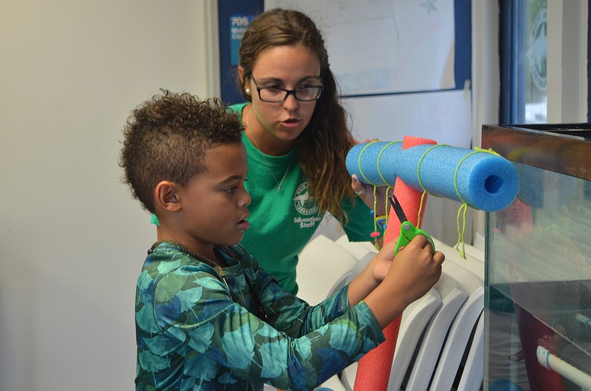 Rainia Lardas shows Dylan Hall, 7, how to hang pretend staghorn coral on a fake coral tree.