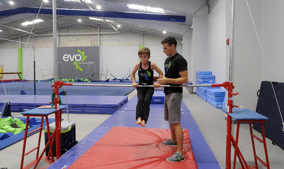 Clayton Spencer, a 2015 graduate of Lakewood Ranch High, works with 8-year-old Nathan Callahan on a cast handstand to back hip circle. After reaching Level 10 status, Spencer is now turning his attention to coaching at EVO Athletics.