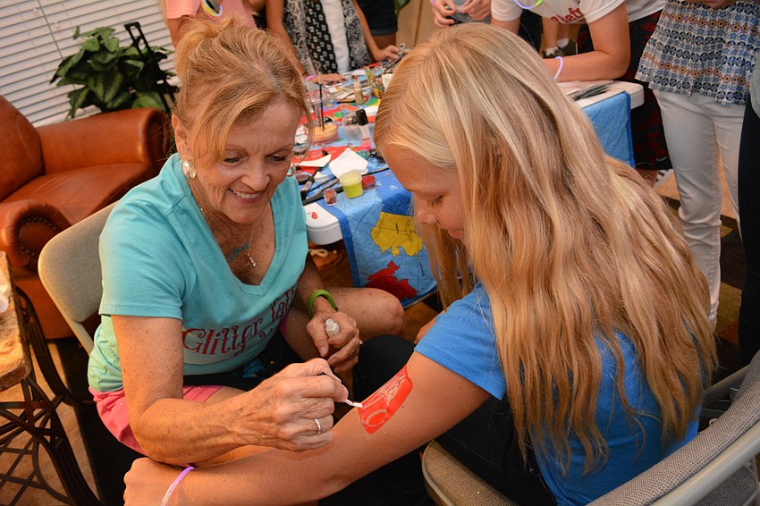 Glitter tattoo artist Judy Sherako perfects a softball tattoo on the arm of Addyson Bruneman, 11.