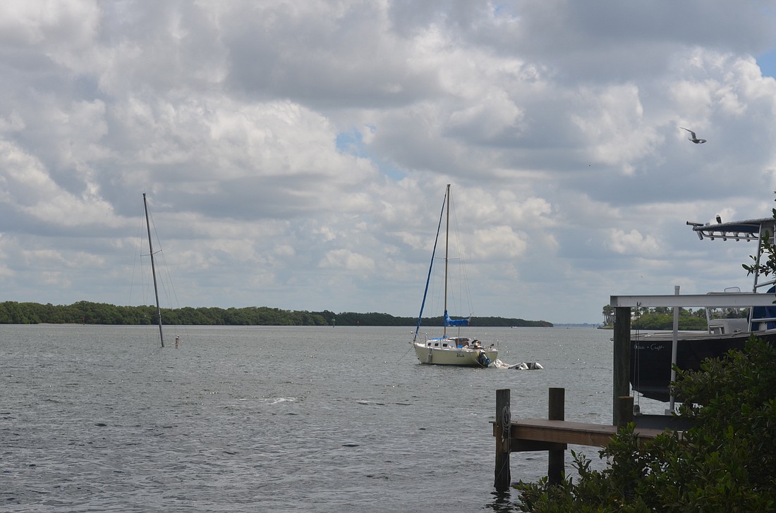 The mast of a sunken sailboat is visible to the left of another vessel in Sarasota Bay.