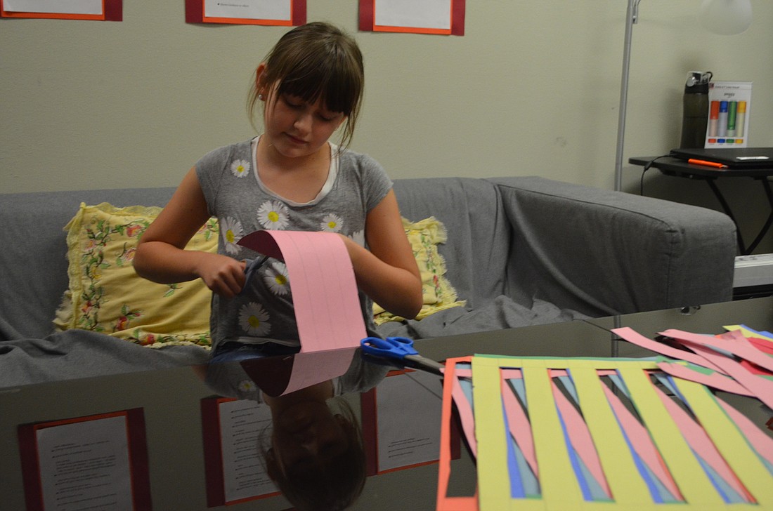 Sienna Hanson, 9, cuts strips of colored paper for her paper-woven iconcept jr. dress at Girls Inc. Photo by Niki Kottmann.