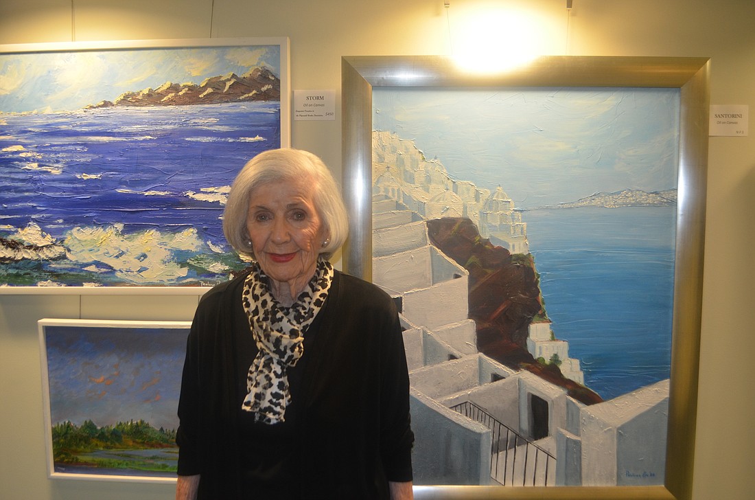 Pauline Nichols stands with some her paintings in the Wellness Center Art Corridor of Plymouth Harbor.