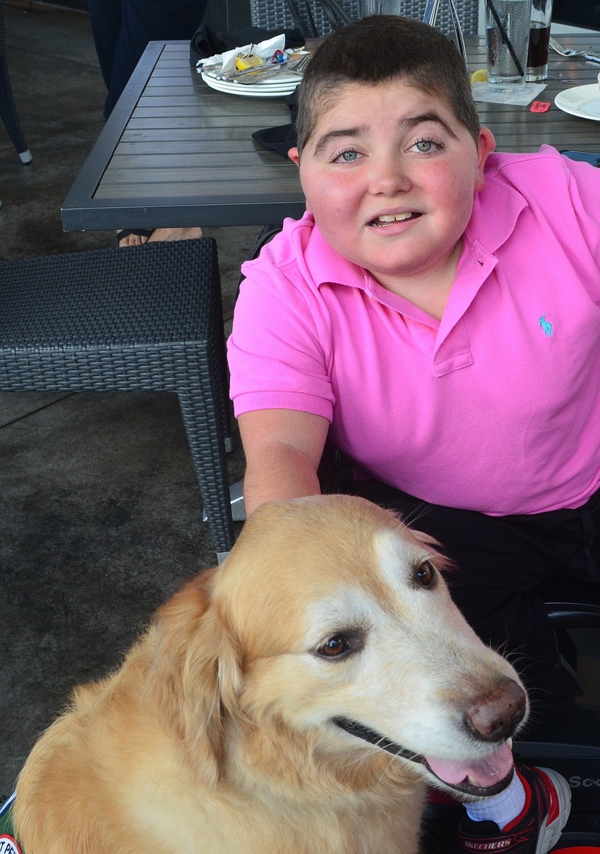 Lakewood Ranch's Grayson Tullio, 13, sits with his service dog Hooch at the Giving Challenge.