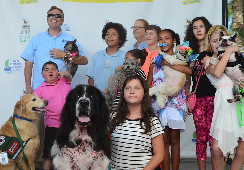 A group of kids, volunteers and dogs sit on the red carpet for a group photo at the Giving Challenge.