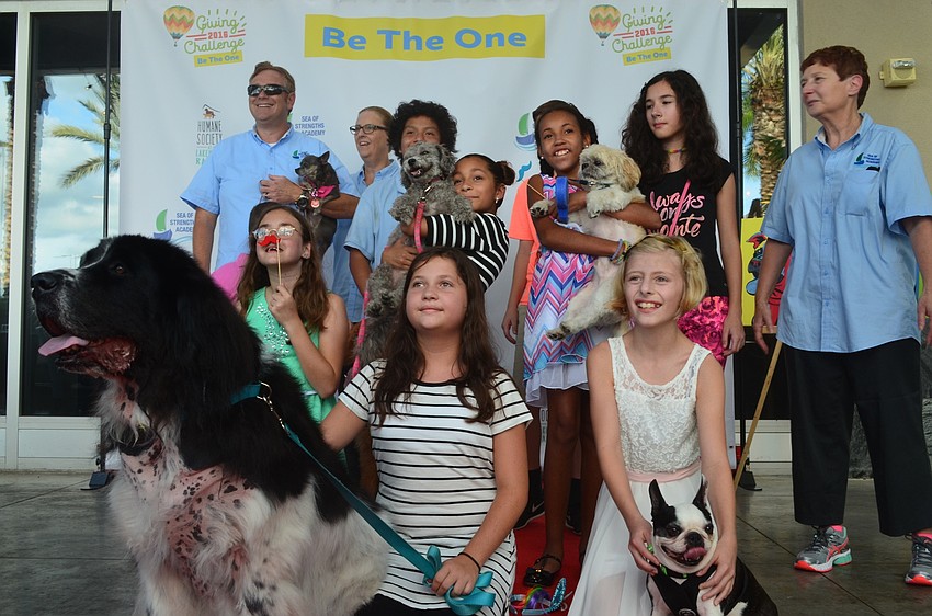 A group of people with their dogs stand on the red carpet for the Giving Challenge at Kona Grill.