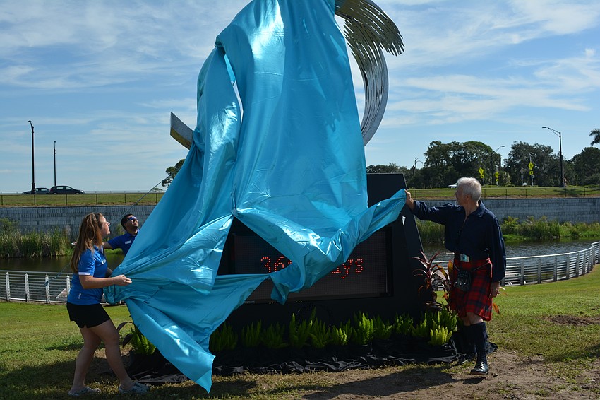 Meredith Scerba, the event director, and artist Malcolm Robertson, rip the covering off the sculpture, 