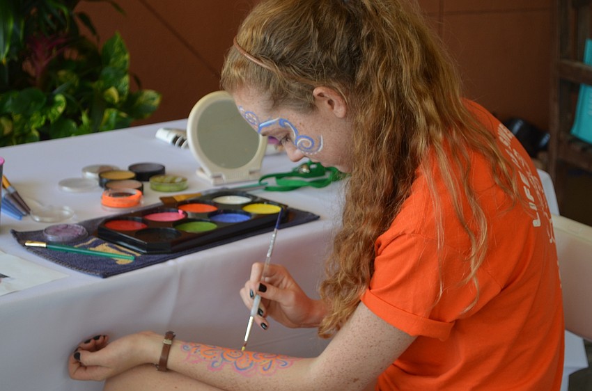 Rosie McClure, 18, paints her arm between her face painting duties at the Health and Wellness Expo.