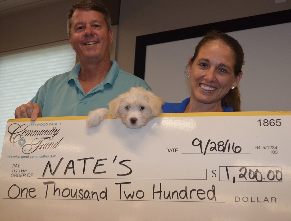 Rob Oglesby, development director at Nate's Honor Animal Rescure, and his wife Dari Oglesby, executive director at Nate's, hold their $1,200 check received from Cheers for Charity as Creamer, the pup, manages to sneak into the photo.