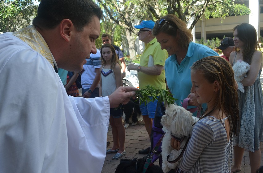 Father Chris Wood blesses maltese, Scooter, while Liza Strong, 10, holds him.