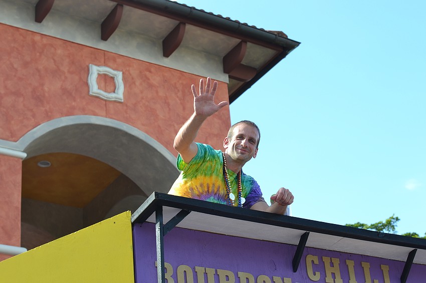 Jason Foltz waves from the second floor of the Station 11 Mardi Gras themed booth.
