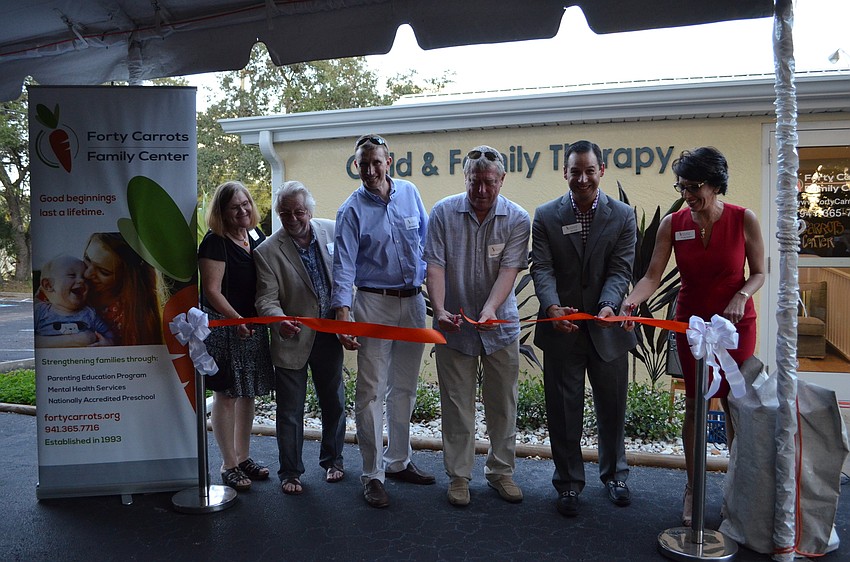 Executive Director Michelle Kapreilian, right, receives help cutting the ribbon from Nancy DeLong, David Jemison, Jeff Steinwachs, Frank Brunckworst and Rick Gomez.