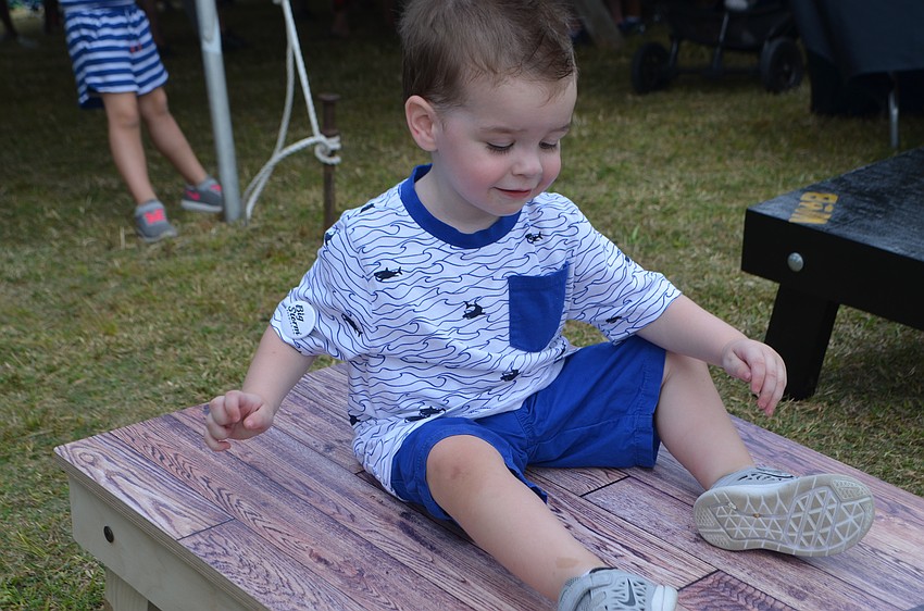 Luke Owens, 2, uses a cornhole board as a slide during Sip the Sunshine.
