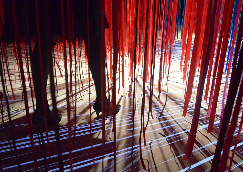 Guests cross laser beams reflected across the floor in the “Pathless Woods” exhibit.