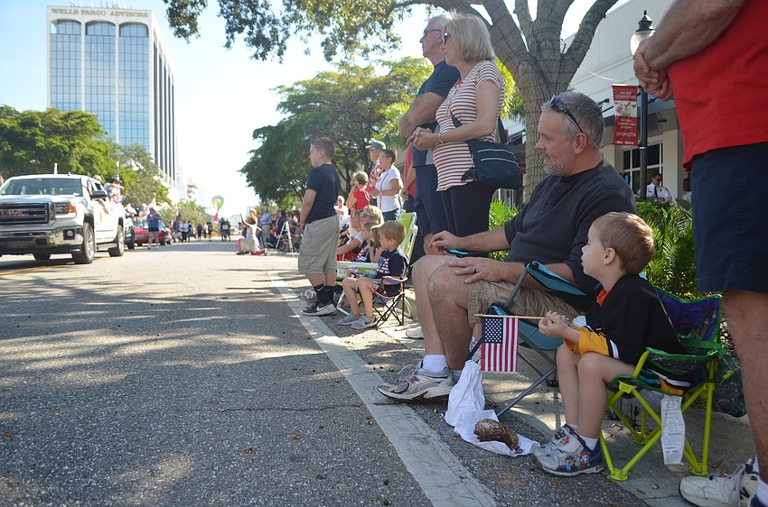 Chris Cabana and Brady Cabana, 4, sit along Main Street, watching the veteran's procession during Sarasota's Veterans Day parade.