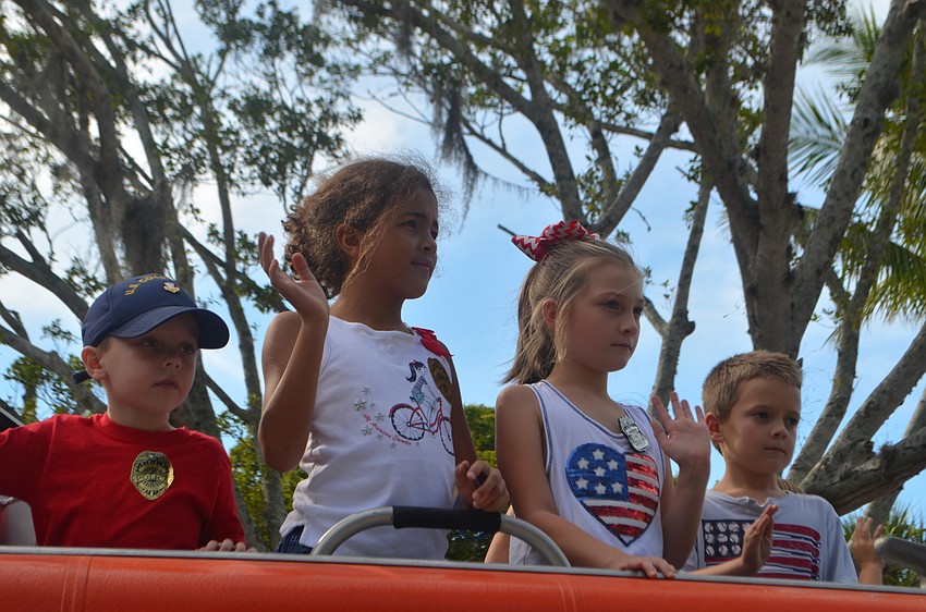 Children wave to the crowd as they ride on a U.S. Coast Guard boat during the third annual Longboat Key Veterans Day Parade.