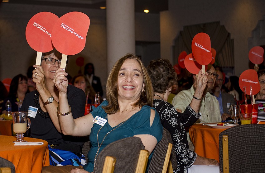 Maria Buitrago raises her paddle during All Faiths Food Bank'  s spin on the tradition paddle raise. Guests used the paddles to indicate past participation in the Campaign Against Summer Hunger.