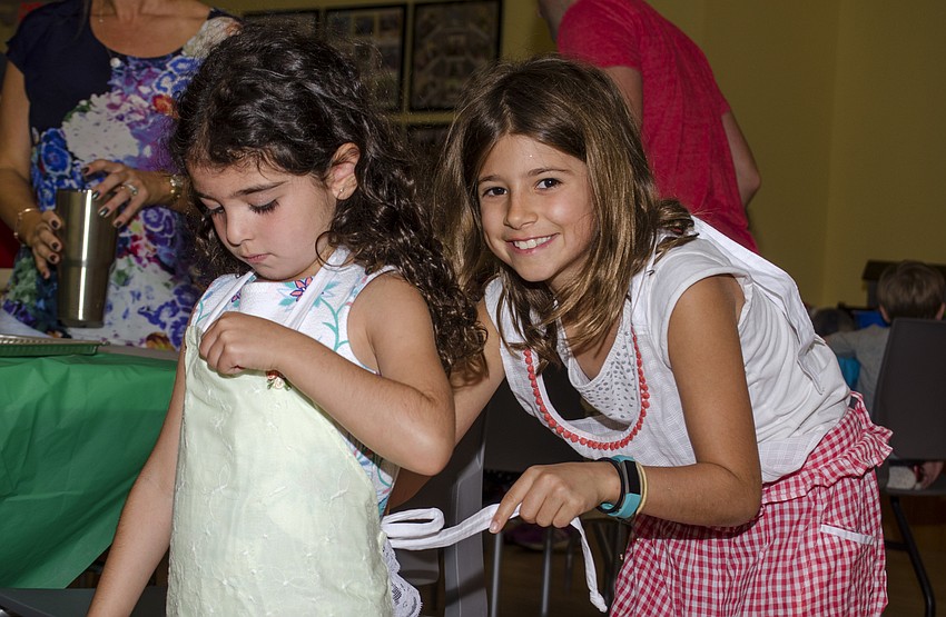 Reese Stroud ties Ariana Ackerman' s apron before the challah workshop.