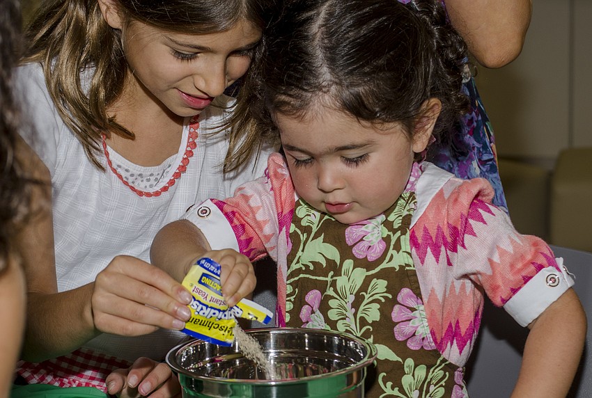 Sienna Ackerman pours yeast into a mixing bowl at the challah workshop at Temple Emanu-El