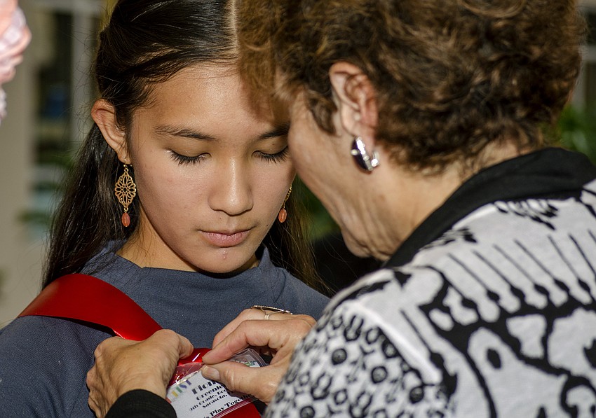 Alice Cotman pins a replica of Booker High School freshman Fiona Greenleaf piece, which is featured in the Embracing Our Differences art exhibition.