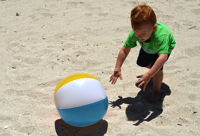 Bryson Heath, 3, chases a beach ball around the sand volleyball court.