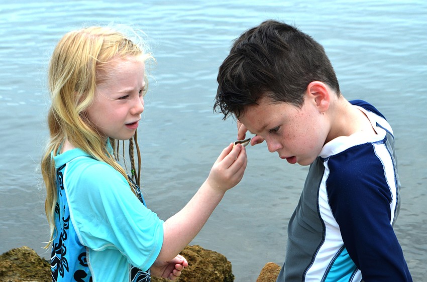 Makenne Marks and Ryan Dascenzl listen for the ocean in seashells they found around New Pass Inlet.