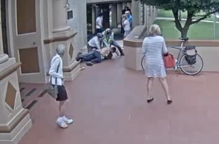 In this shot from the St. Martha Catholic Church security camera footage, City Manager Tom Barwin and two others are seen restraining the man as church goers gather around the scene.