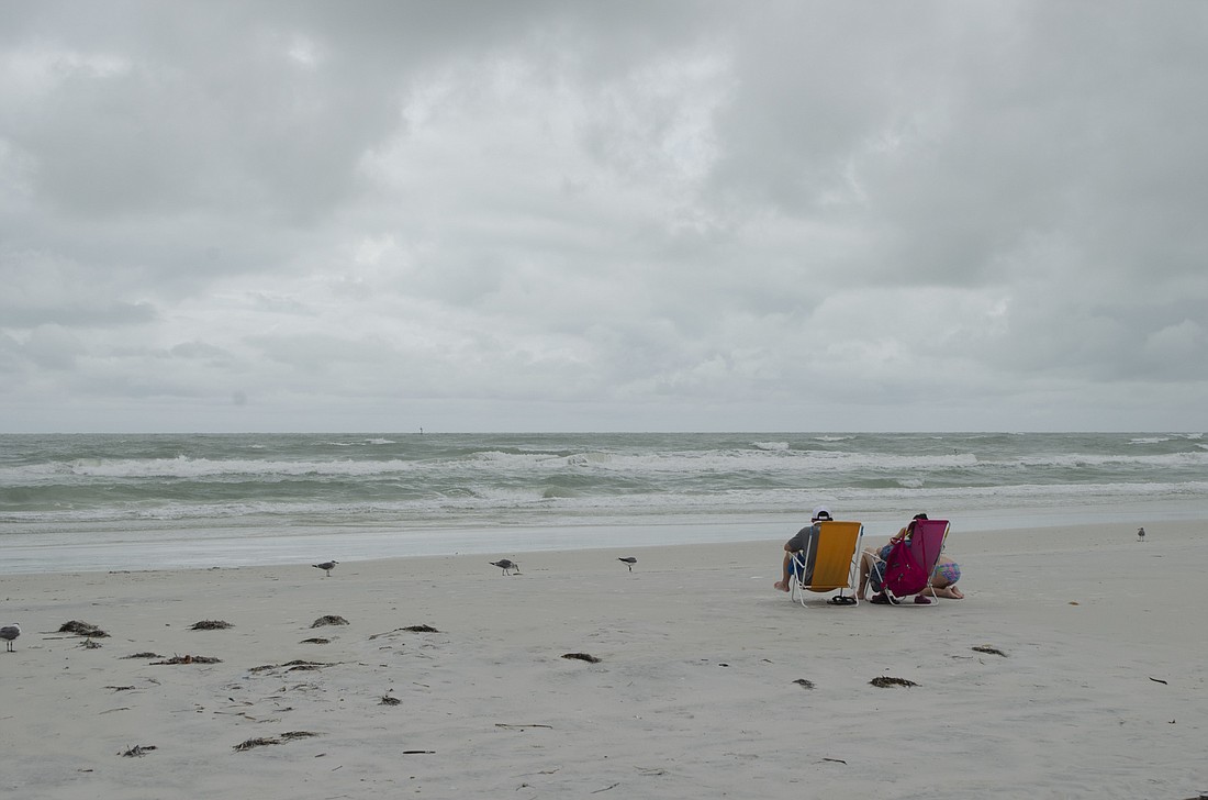 A small family sits on the beach watching the waves brought on by Tropical Storm Emily.