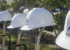 Hard hats with The Mark logo printed on their fronts sit on shovels before the ground breaking.