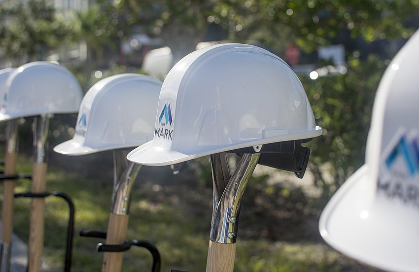 Hard hats with The Mark logo printed on their fronts sit on shovels before the ground breaking.