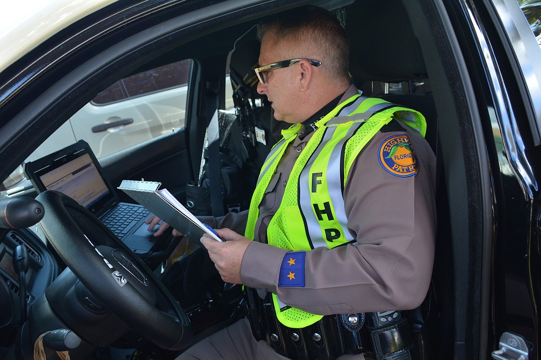 Florida Highway Patrol Trooper Kenn Watson checks for information updates while on scene, parked in parking area of Main Street at Lakewood Ranch by Starbucks.