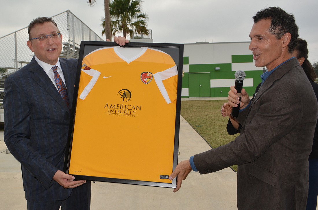 Bob Ritchie, the president and CEO of American Integrity Insurance, accepts a Chargers jersey with his company logo on it from Premier Sports Director Antonio Saviano.