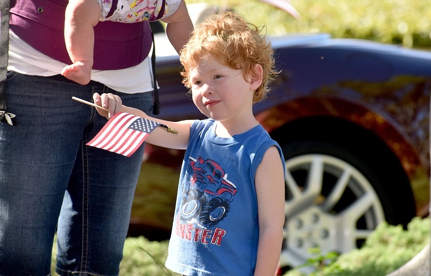 Phoenix Harwood waves an American flag as veterans walk past him during the parade.