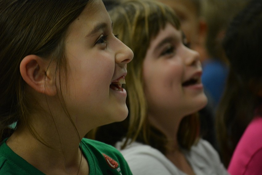 Third graders Gaby Papageorgiou and Emma Cappelluti smile as a first-graders start a song they know.