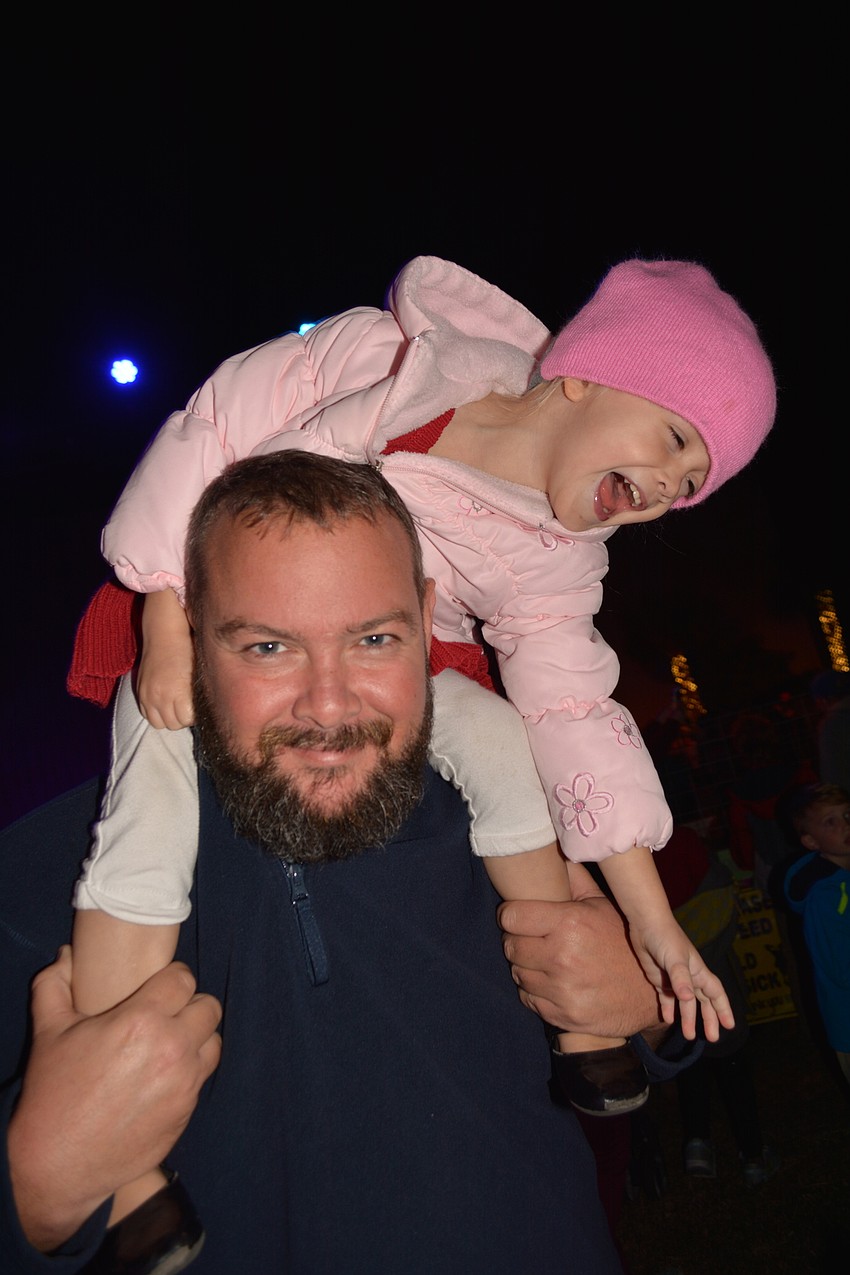 Sofia Evans, 3, dives toward her feet as her mom, Shannon, not pictured, tickles them. She rides on the shoulders of her dad, Derek, because of the crowd.