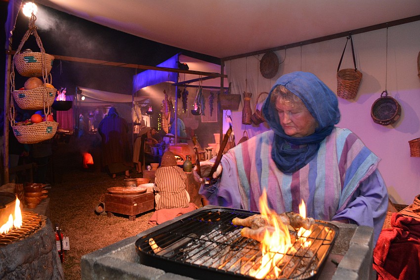 Actress Irene Carol cooks chicken legs over an open flame at one of the interactive sets.