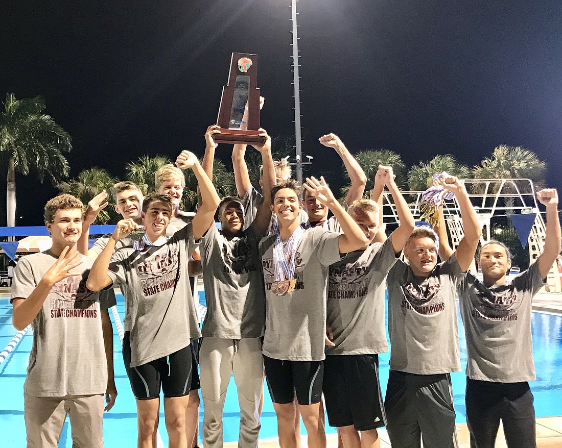 The Riverview High boys swimming team holds aloft its fourth-consecutive state swimming title.