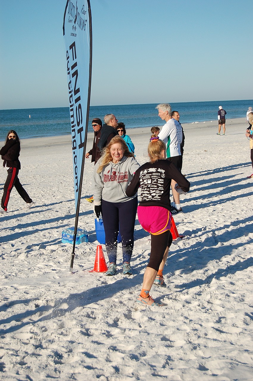 Organizer Stacey Monroe congratulates runners at the finish line on Siesta Beach.