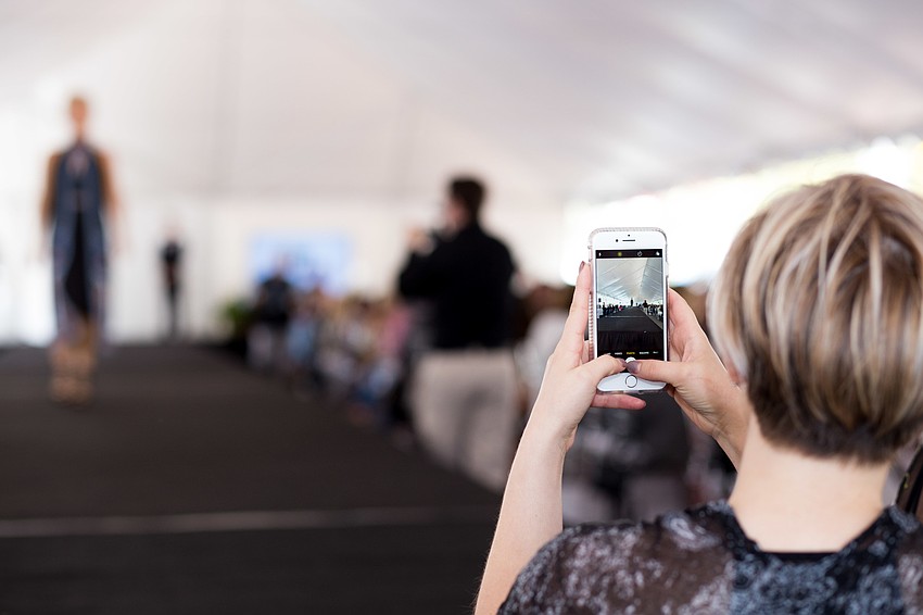 A guest takes a video of the models coming down the runway.
