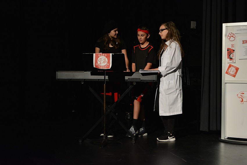 Natalie Carrion, portraying Kelsi Neilsen, the drama club's pianist, shares with Troy Bolton and Gabriella Montez (Johnny Robinson and Madisyn Wandall) the way her song is supposed to sound when performed.