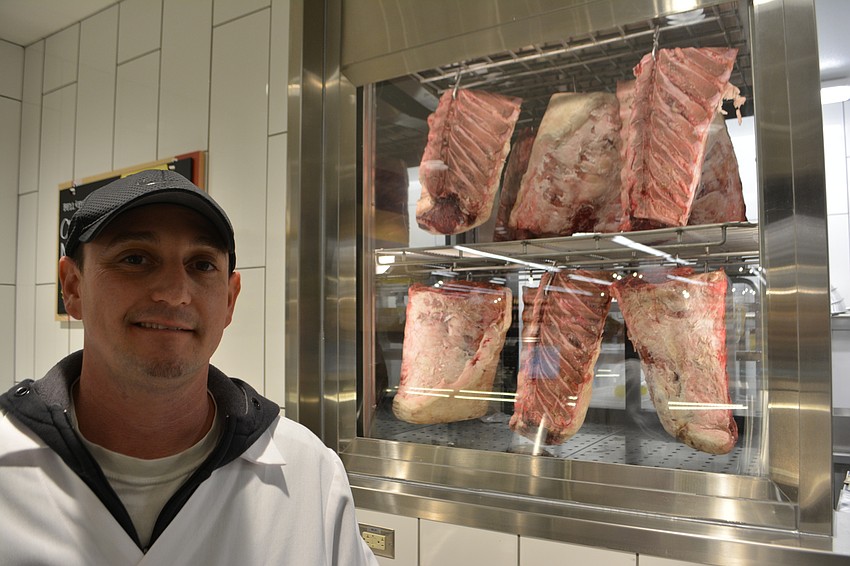Meat Associate Team Leader Drew Magnoli stands in front of dry aged rib-eyes, which hang for at least 14 days from a hook that helps them break down muscles and fibers.
