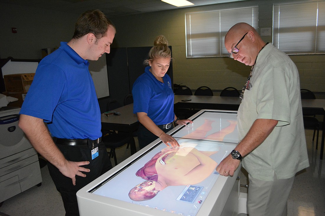 MTC paramedic students Nick Treffinger and Lydia Wilkinson work on the Anatomage table with Jay Bush, the Emergency Medical Services program director at MTC.