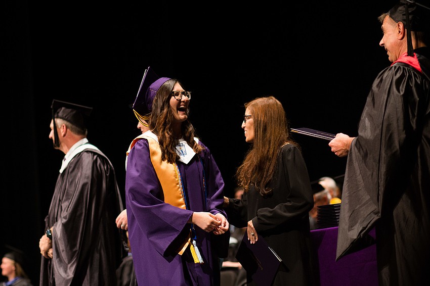 Shaking hands with a faculty member, a graduate walks to get her diploma.