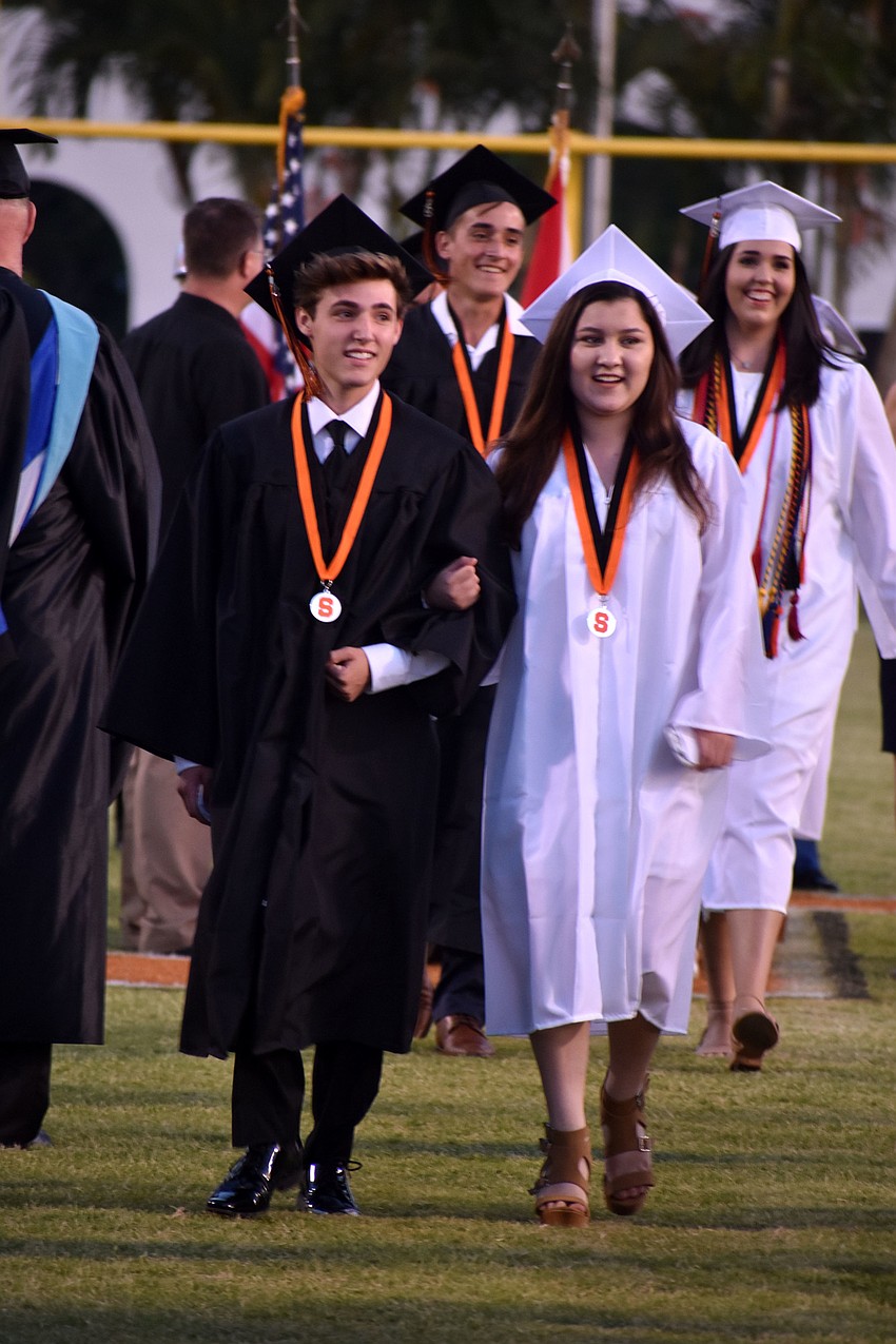 Graduates are all smiles as they walk to their seats on the football field.