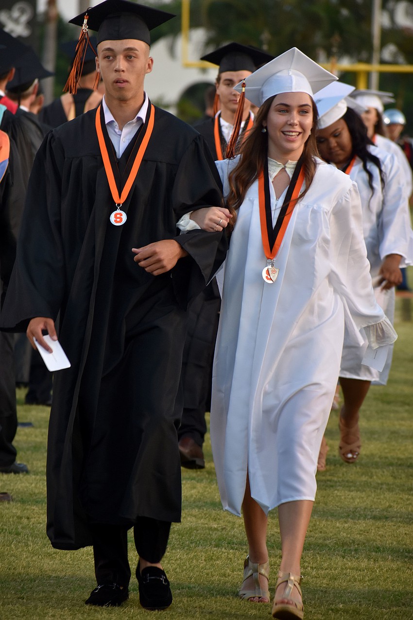 Graduates are all smiles as they walk to their seats on the football field.