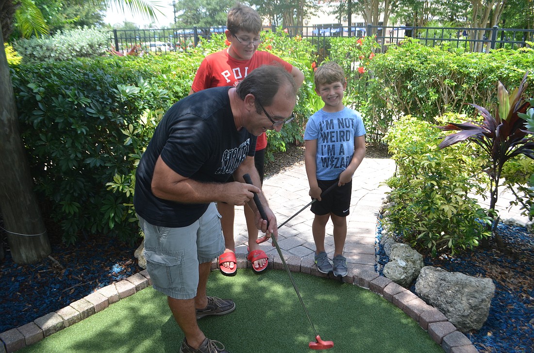 Dylan Zafirov knocks a ball into the hole at the Fish Hole while his sons, Leo, 12, and Michael, 6, cheer him on.