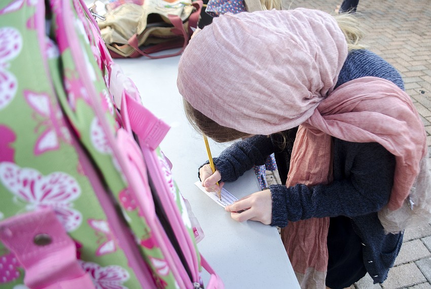 Addie Ross fills out a luggage tag to attach to her bag at the baggage check booth at Phillippi Shores Elementary School’s mock Ellis Island.